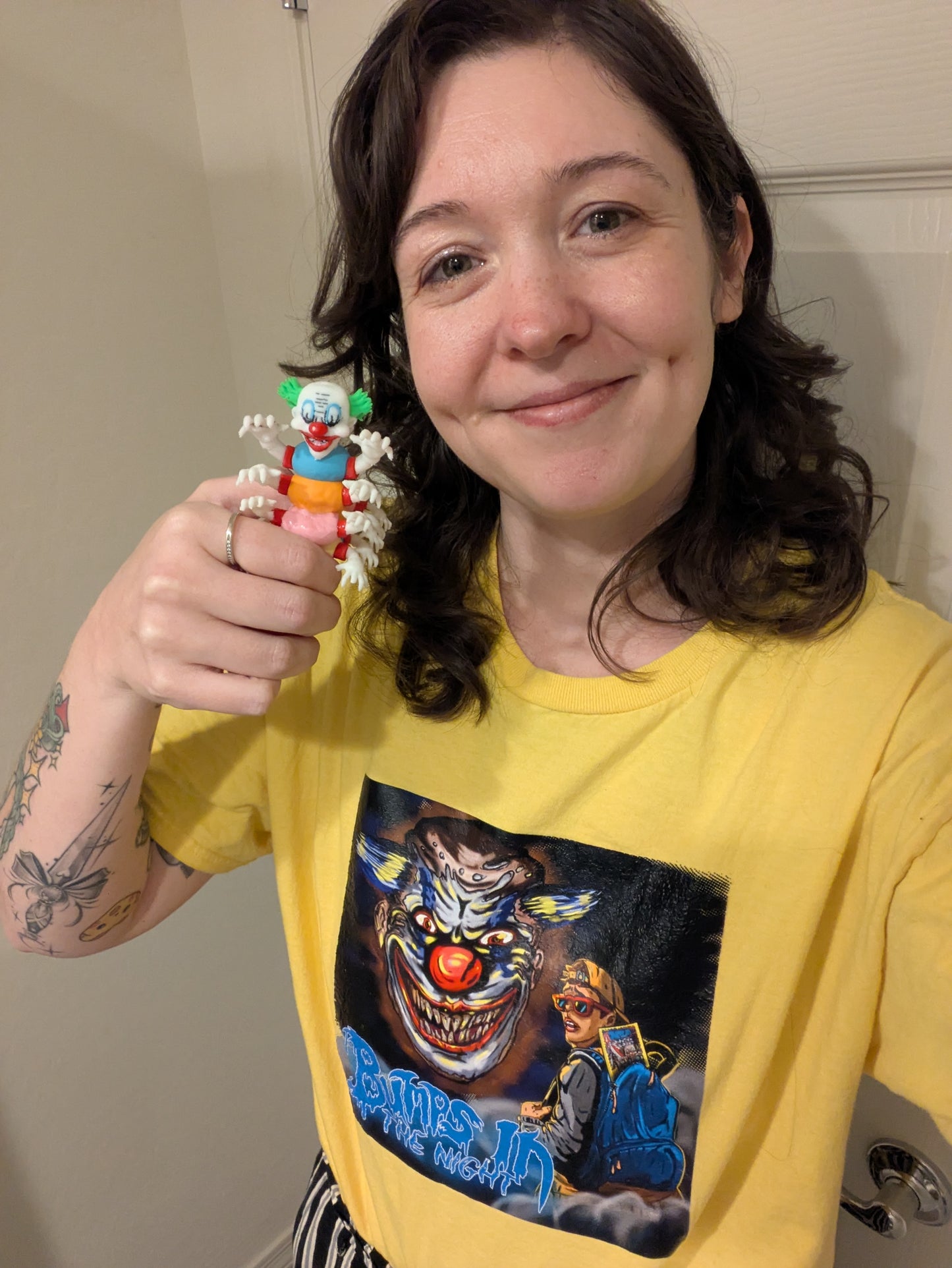 Person wearing a yellow t-shirt with a graphic design, holding a small clown figurine.